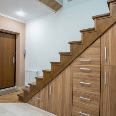 Modern architecture interior with luxury hallway with glossy wooden stairs in multi-storey house. Custom built pullout cabinets on glides in slots under stairs. Use of space for storage.